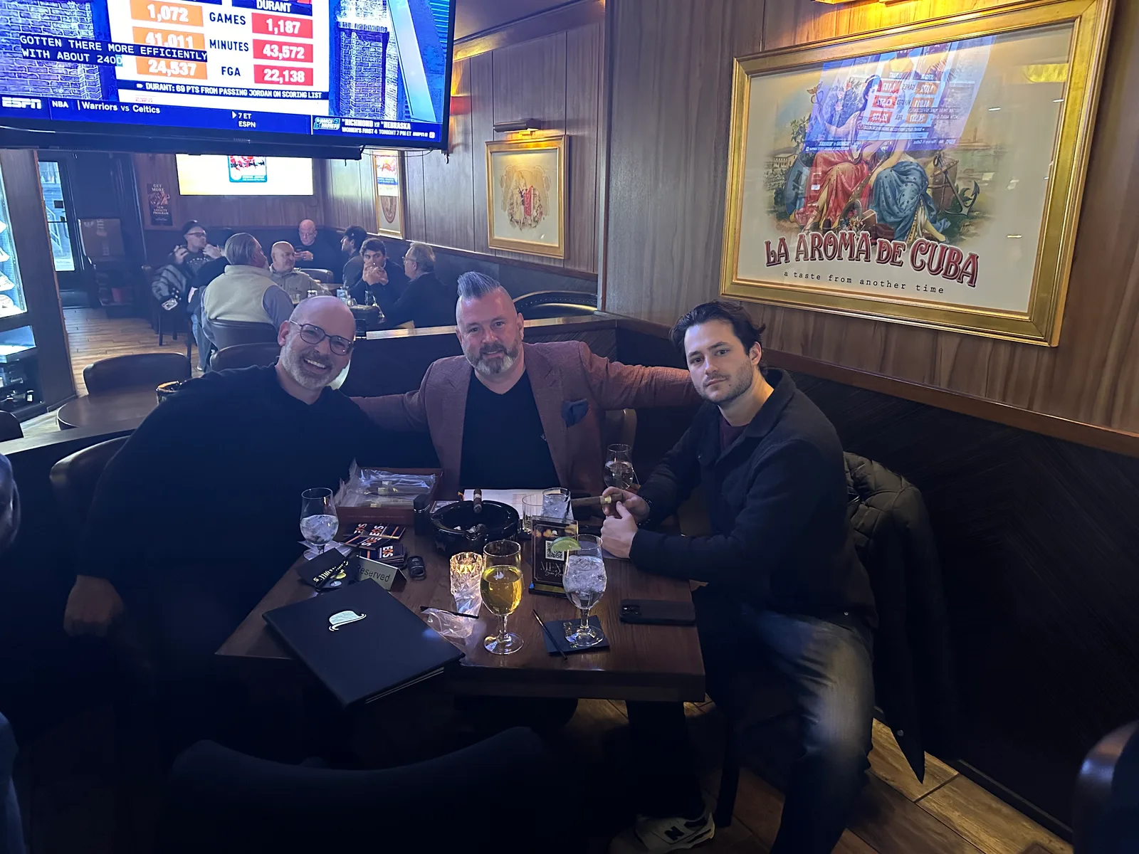 Three friends seated together with cigars and drinks at a lounge table