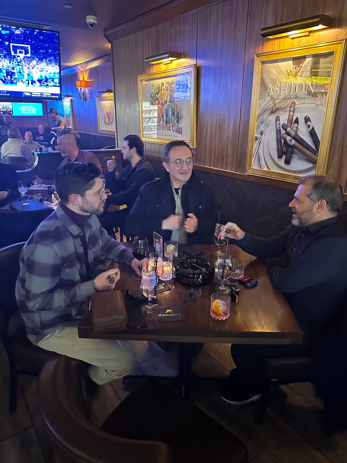 Guests sharing conversation and cigars around a table in a wood-paneled lounge