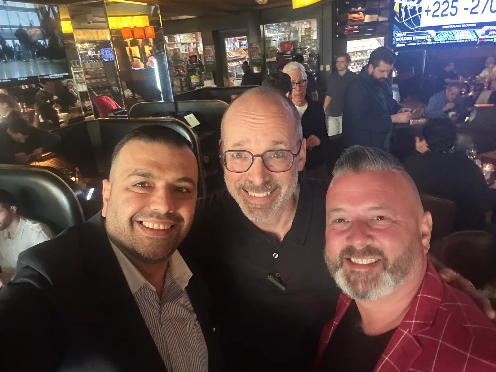 Three friends smiling for a selfie at a busy cigar lounge gathering